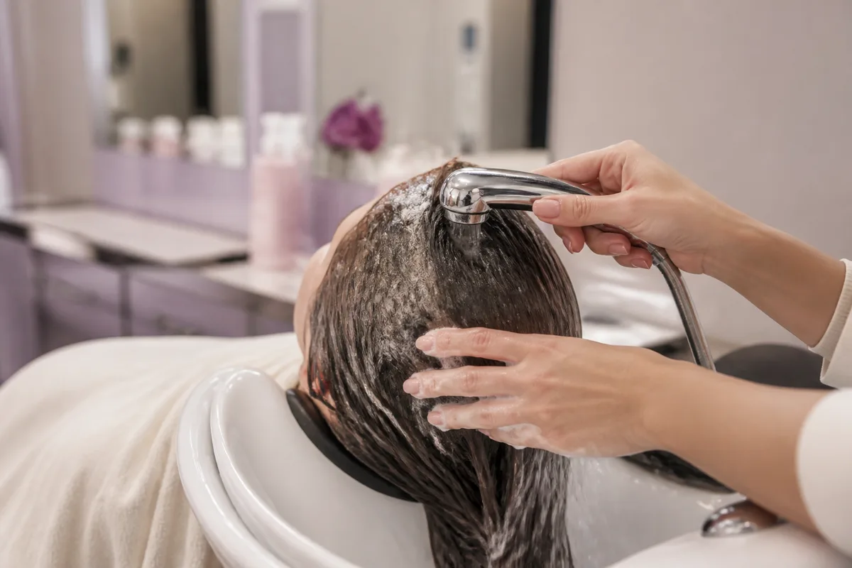 Application du shampoing sur le cuir chevelu du bout des doigts sous la douche