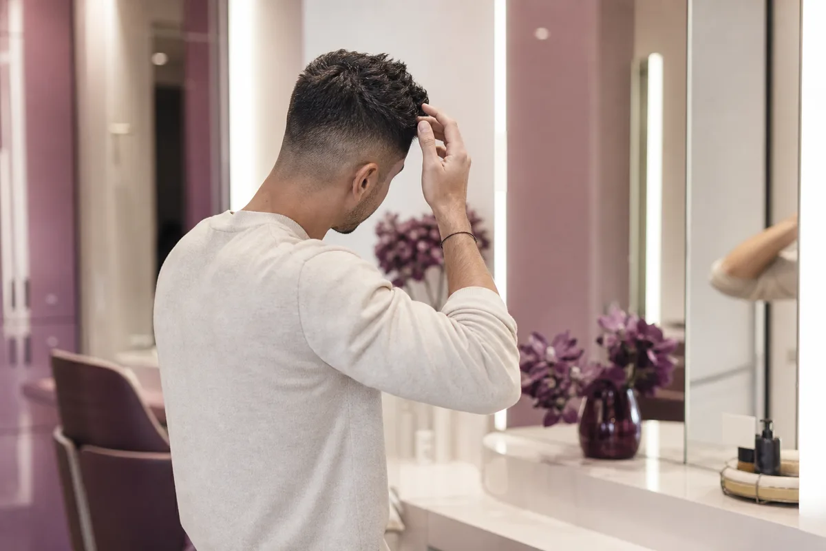 Homme se coiffant devant un miroir quelques jours après une coupe dégradée